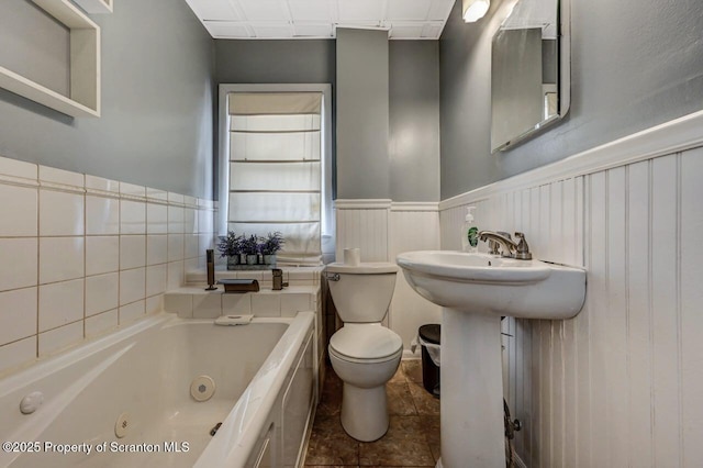 bathroom with a whirlpool tub, wainscoting, and toilet