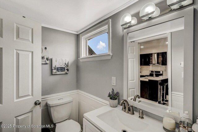 half bath with a wainscoted wall, a decorative wall, vanity, and toilet