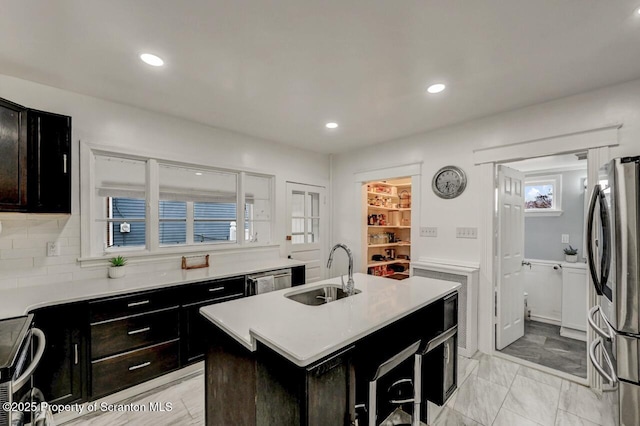 kitchen with appliances with stainless steel finishes, a kitchen island with sink, light countertops, and a sink