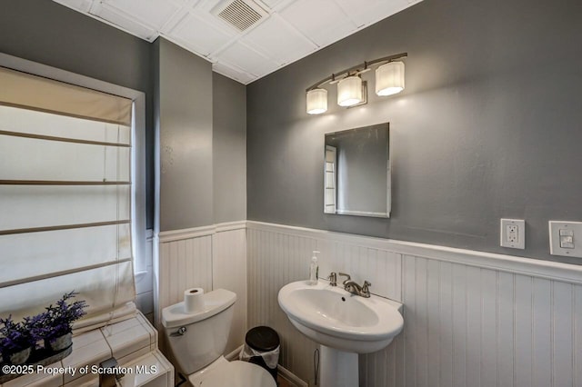 bathroom with a wainscoted wall, toilet, a sink, and visible vents