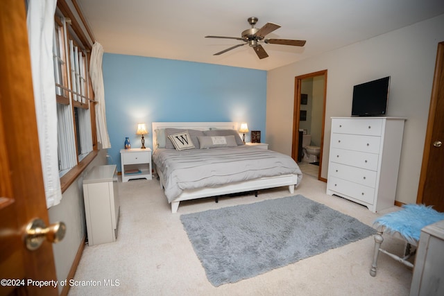 bedroom featuring ceiling fan, light colored carpet, and connected bathroom