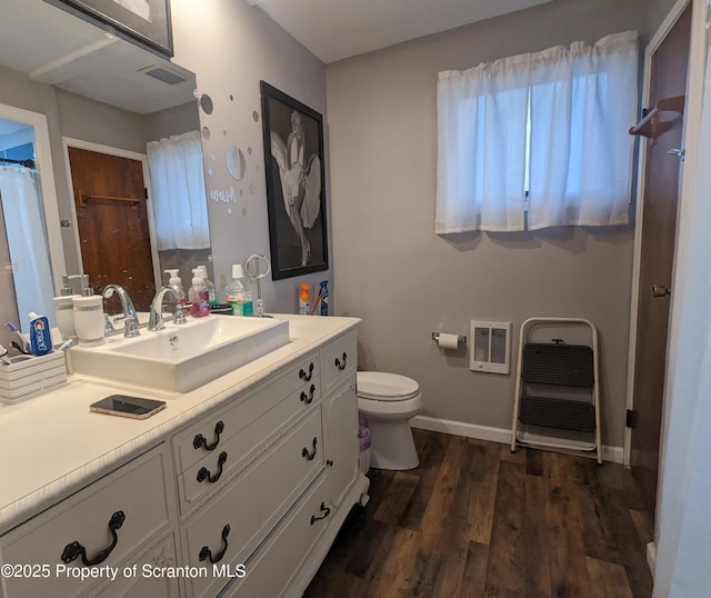 bathroom featuring heating unit, wood-type flooring, toilet, and vanity