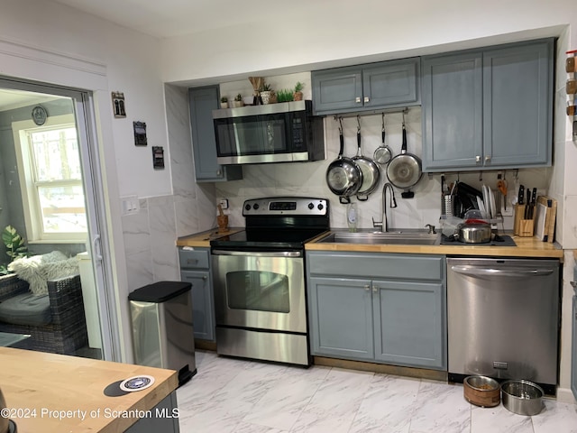 kitchen with gray cabinetry, sink, tasteful backsplash, butcher block countertops, and appliances with stainless steel finishes