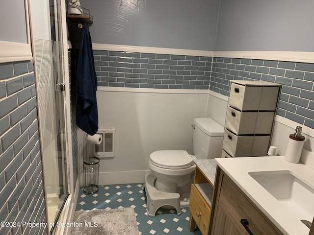 bathroom with vanity, toilet, tile walls, and a shower with shower door