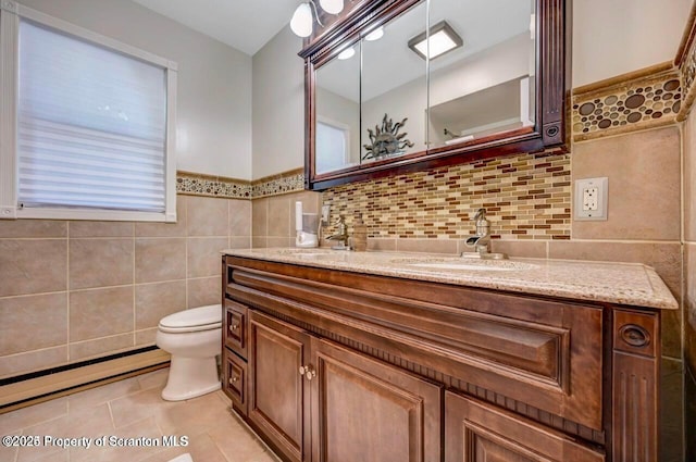 bathroom with baseboard heating, tile patterned flooring, toilet, vanity, and tile walls