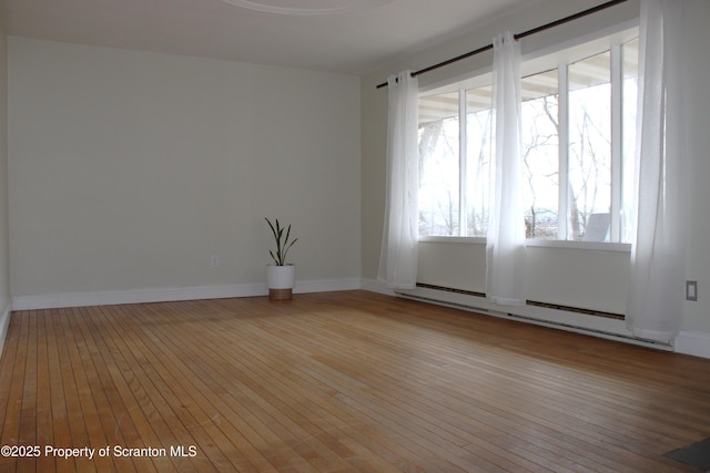 unfurnished room with a baseboard heating unit and light hardwood / wood-style floors