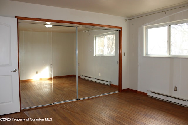 unfurnished bedroom featuring hardwood / wood-style floors, a closet, and a baseboard heating unit