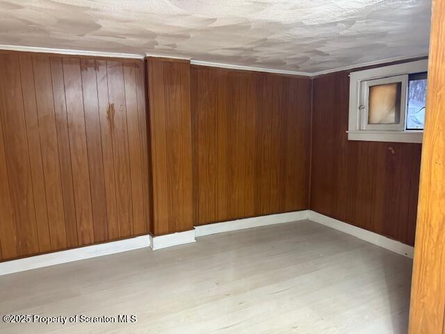 empty room with wood walls, light wood-style flooring, and baseboards