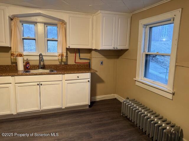 kitchen featuring dark countertops, radiator heating unit, white cabinets, and a sink