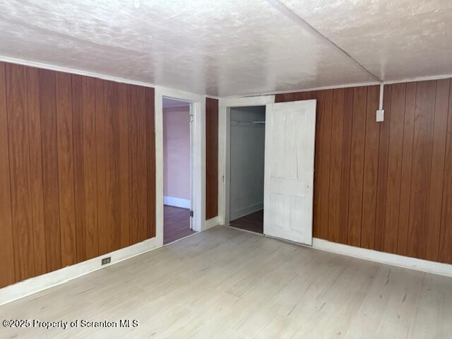 unfurnished bedroom featuring light wood-type flooring, a closet, wooden walls, and baseboards