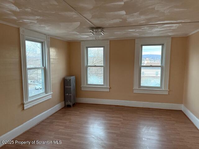 empty room featuring baseboards, radiator heating unit, and wood finished floors