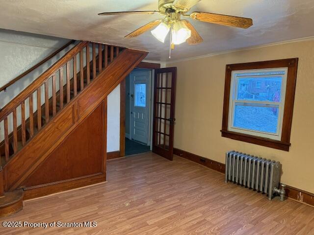 interior space featuring radiator, ornamental molding, wood finished floors, baseboards, and stairs