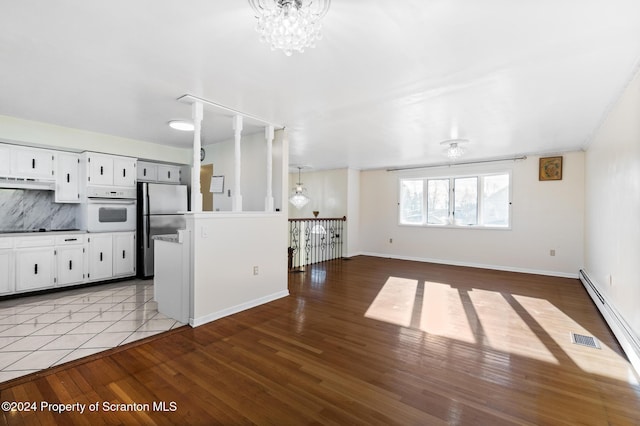 kitchen featuring backsplash, white oven, an inviting chandelier, white cabinets, and stainless steel refrigerator