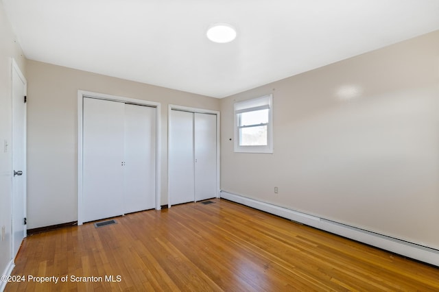 unfurnished bedroom with a baseboard radiator, light hardwood / wood-style flooring, and multiple closets