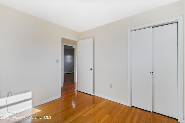 unfurnished bedroom featuring light wood-type flooring, a closet, and a baseboard heating unit