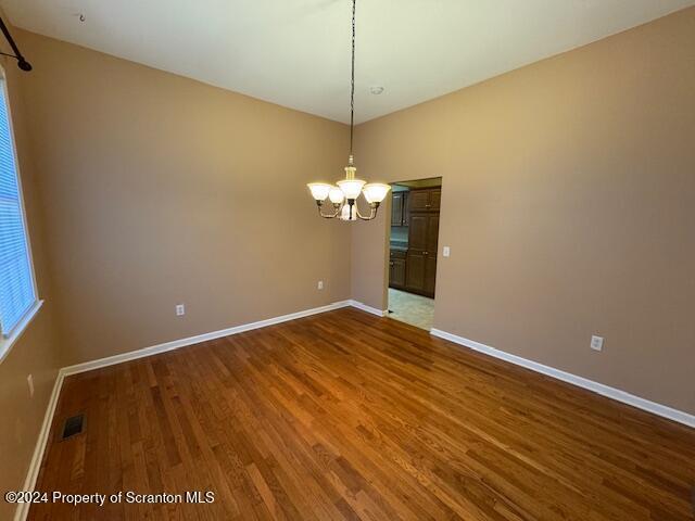 empty room featuring a notable chandelier and wood-type flooring