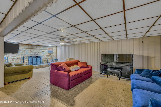 living room featuring a stone fireplace, ceiling fan, and a paneled ceiling