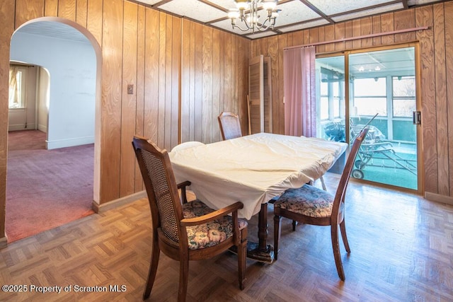 dining area featuring an inviting chandelier, parquet floors, and wooden walls