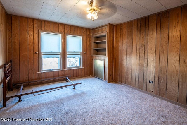 unfurnished room featuring built in features, light carpet, wood walls, and ceiling fan