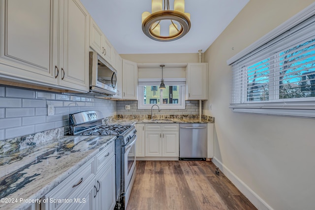 kitchen with light stone countertops, stainless steel appliances, sink, white cabinetry, and hanging light fixtures