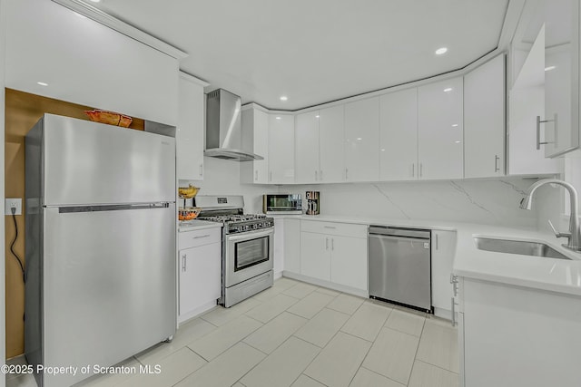 kitchen with wall chimney range hood, a sink, white cabinetry, and appliances with stainless steel finishes