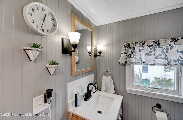 bathroom with a textured ceiling, vanity, crown molding, and wood walls