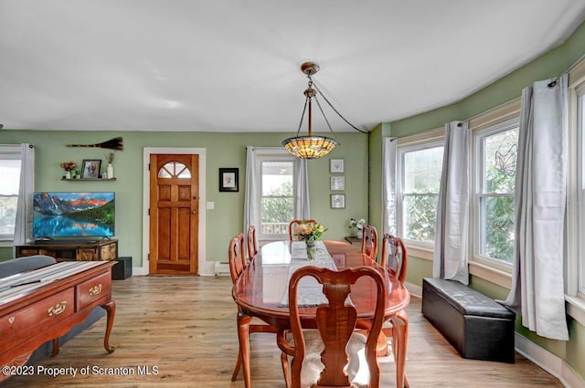 dining room featuring baseboard heating, light hardwood / wood-style flooring, a healthy amount of sunlight, and an inviting chandelier