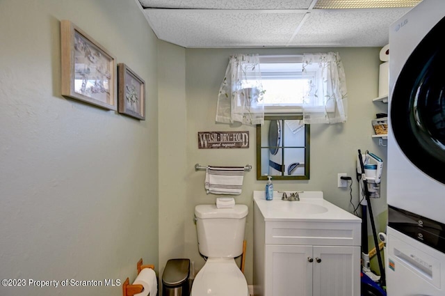 bathroom with a paneled ceiling, stacked washer and dryer, vanity, and toilet