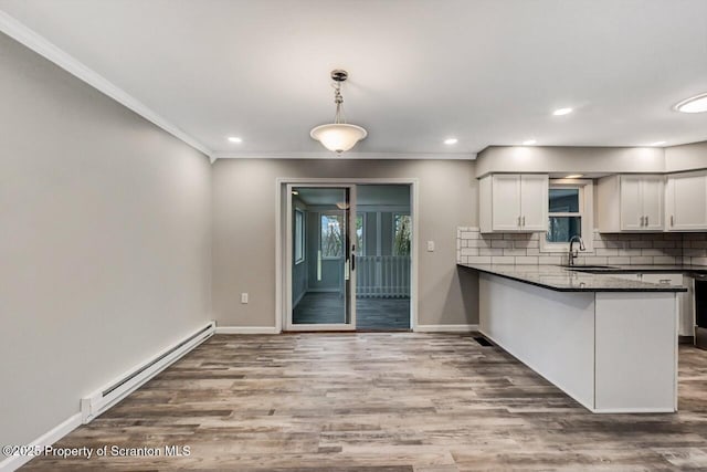 kitchen with a baseboard heating unit, kitchen peninsula, sink, decorative light fixtures, and white cabinetry