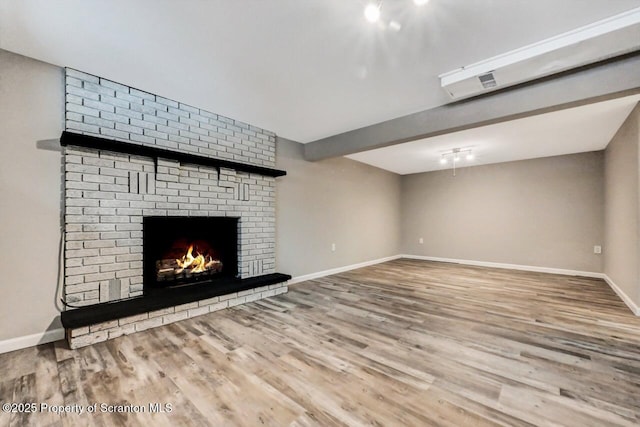 unfurnished living room with wood-type flooring and a brick fireplace