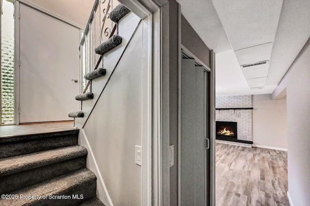 stairway with wood-type flooring and a brick fireplace