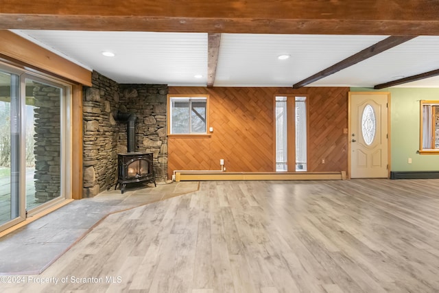 unfurnished living room featuring a wood stove, wooden walls, light hardwood / wood-style flooring, and a baseboard radiator