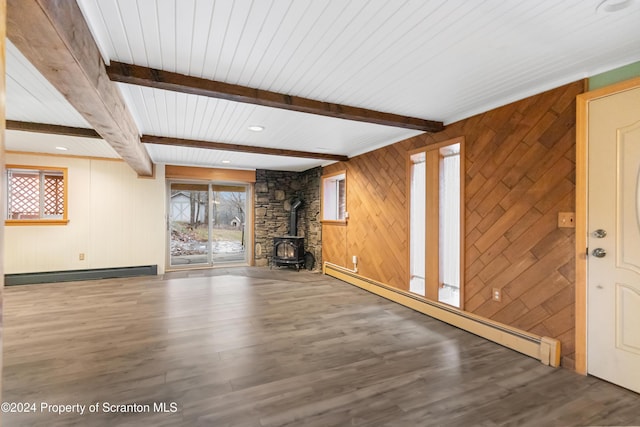 unfurnished living room with beam ceiling, a wood stove, baseboard heating, and wooden walls