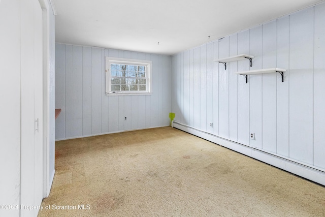 empty room with wood walls, baseboard heating, and light carpet