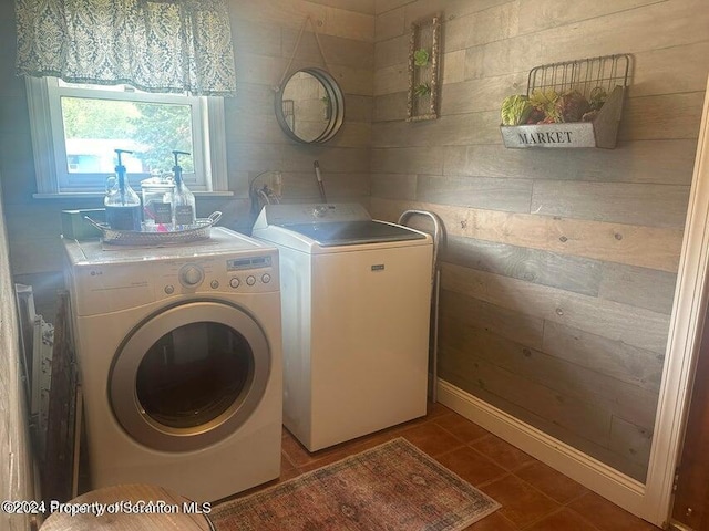 clothes washing area featuring tile patterned floors, washing machine and dryer, and wooden walls