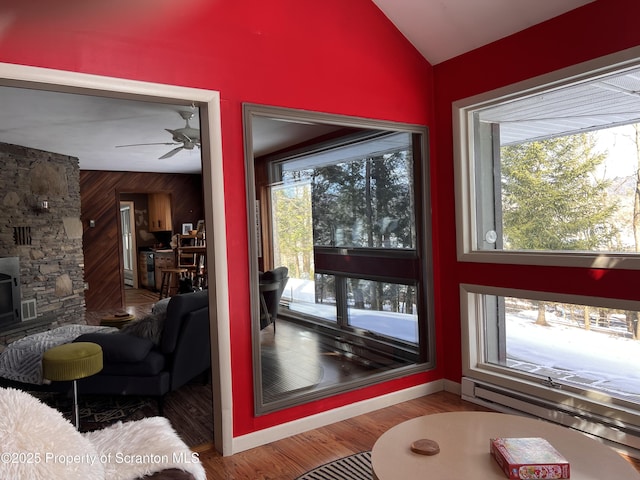 doorway featuring wooden walls, lofted ceiling, a wood stove, hardwood / wood-style flooring, and ceiling fan