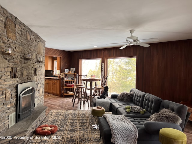 living room featuring hardwood / wood-style floors, a stone fireplace, wooden walls, and ceiling fan