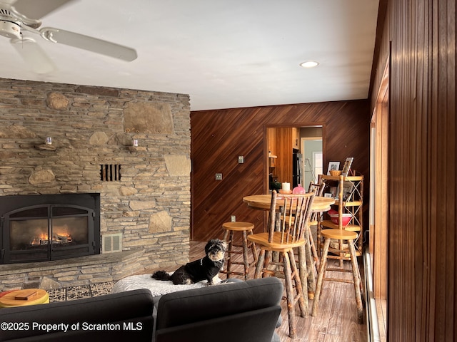 living room featuring ceiling fan, wood-type flooring, a fireplace, and wood walls