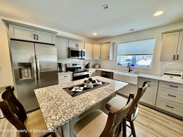 kitchen featuring stainless steel appliances, a center island, a kitchen breakfast bar, and light stone counters