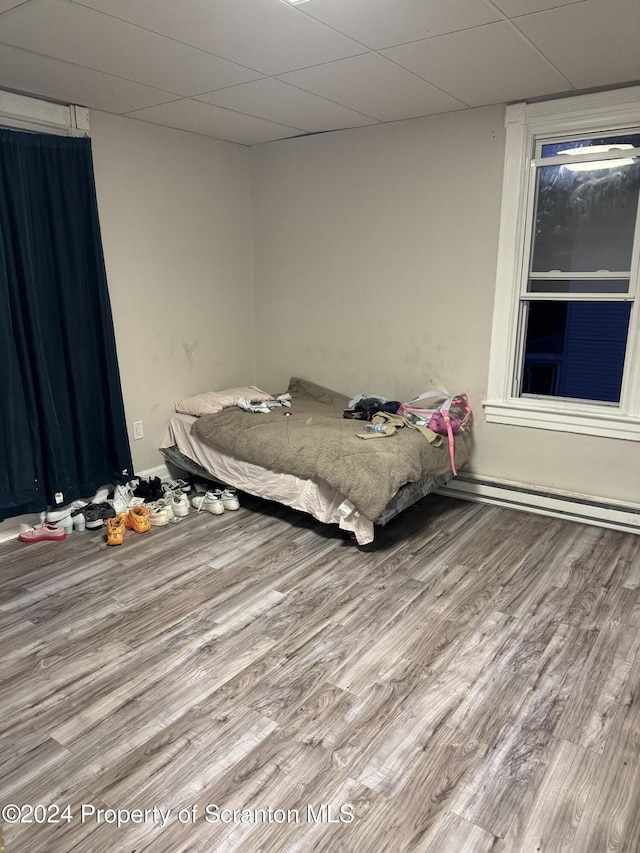 unfurnished bedroom featuring baseboard heating, a paneled ceiling, and hardwood / wood-style floors