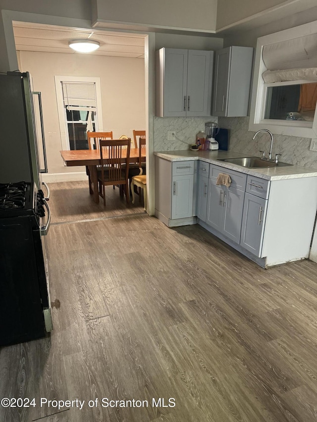 kitchen featuring black gas range, dark wood-type flooring, refrigerator, sink, and gray cabinets