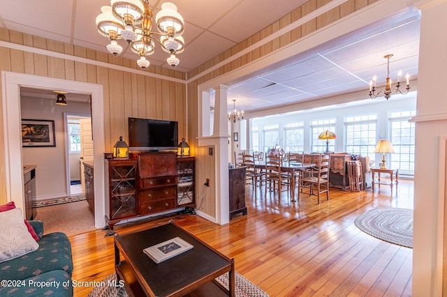 living area featuring a notable chandelier, wood walls, a paneled ceiling, and wood-type flooring