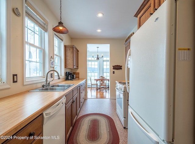 kitchen with a sink, white appliances, brown cabinetry, and hanging light fixtures