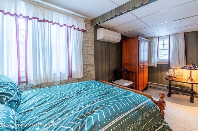 carpeted bedroom with a paneled ceiling, wooden walls, and a wall mounted AC