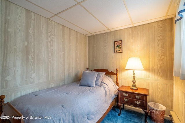 bedroom with a paneled ceiling, carpet, and wood walls