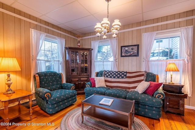 living area featuring hardwood / wood-style flooring, a paneled ceiling, wood walls, and a chandelier