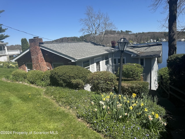 view of side of home with a chimney, a yard, and roof with shingles