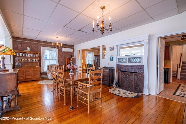 dining area featuring a wall mounted air conditioner, stairs, hardwood / wood-style floors, an inviting chandelier, and a paneled ceiling