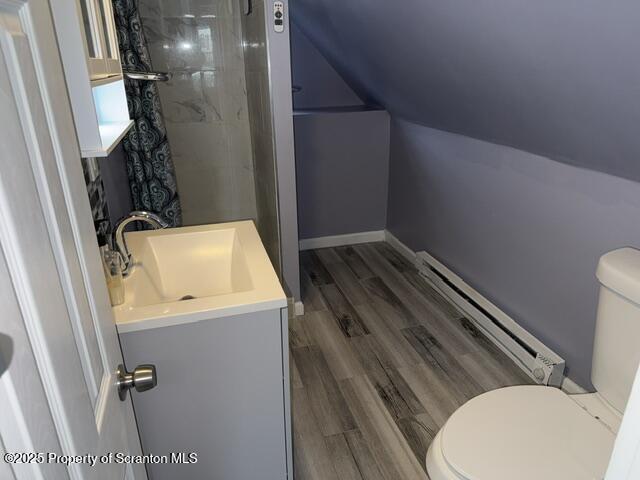 bathroom with toilet, wood finished floors, vanity, baseboard heating, and vaulted ceiling
