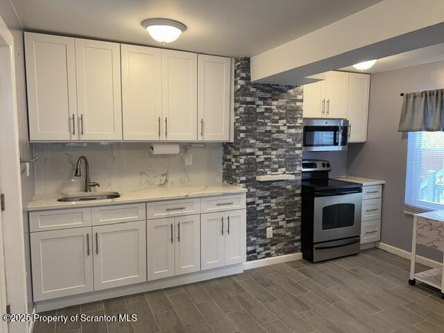 kitchen with white cabinetry, backsplash, a sink, appliances with stainless steel finishes, and wood tiled floor